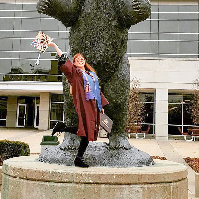 MSU graduate in front of the MSU bear statue